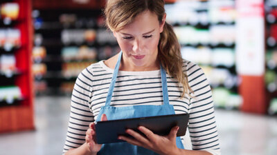 Trainee-Angestellte im Lebensmittelgeschäft mit Tablet in der Hand.